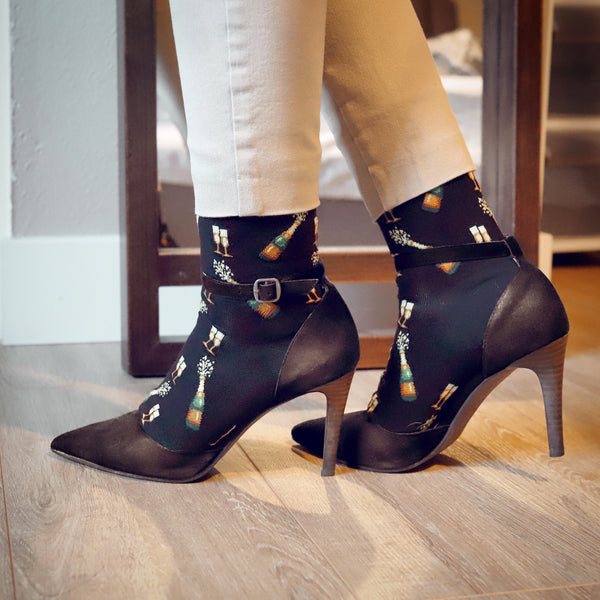 Lifestyle shot of woman's legs wearing black 'Champagne Bottles' socks and brown heels. [lf]