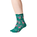 Lifestyle shot: Person wearing dark green crew socks with a pattern of pink flamingos in Santa hats.