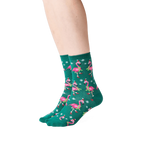 Lifestyle shot: Person wearing dark green crew socks with a pattern of pink flamingos in Santa hats.