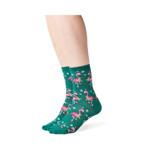Lifestyle shot: Person wearing dark green crew socks with a pattern of pink flamingos in Santa hats.