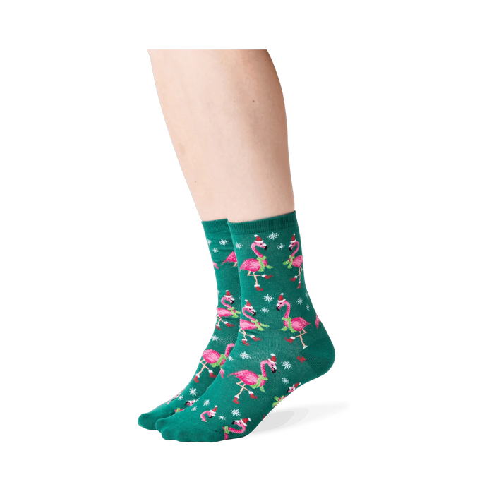 Lifestyle shot: Person wearing dark green crew socks with a pattern of pink flamingos in Santa hats.