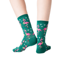Back view of a person's legs wearing dark green crew socks with a pattern of pink flamingos wearing Santa hats.