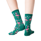 Back view of a person's legs wearing dark green crew socks with a pattern of pink flamingos wearing Santa hats.