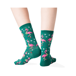 Back view of a person's legs wearing dark green crew socks with a pattern of pink flamingos wearing Santa hats.