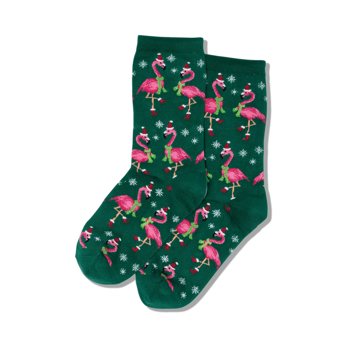 dark green women's crew socks adorned with pink flamingos wearing santa hats and green scarves against a backdrop of white snowflake.  