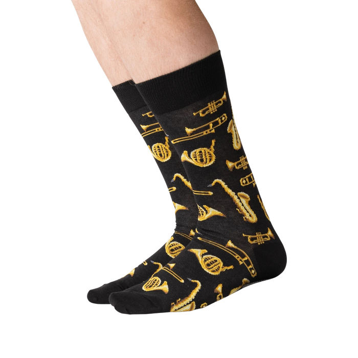 A pair of black socks with a pattern of gold musical instruments, including trumpets, trombones, saxophones, and clarinets.