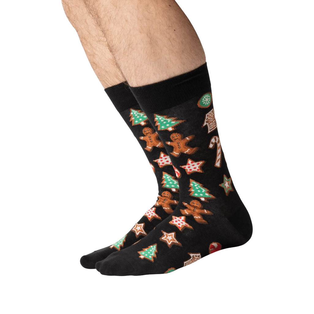 Person's legs wearing black Christmas Cookie socks, shown from the side.