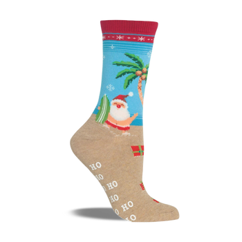 Beige non-skid slipper sock with a red cuff. Features Santa surfing, a palm tree, snowflakes, and presents on a beach scene.