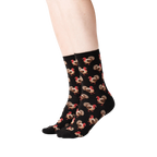 Lifestyle shot of a person's legs wearing black crew socks with a repeating pattern of brown and red turkeys.