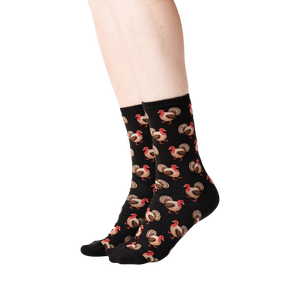 Lifestyle shot of a person's legs wearing black crew socks with a repeating pattern of brown and red turkeys.