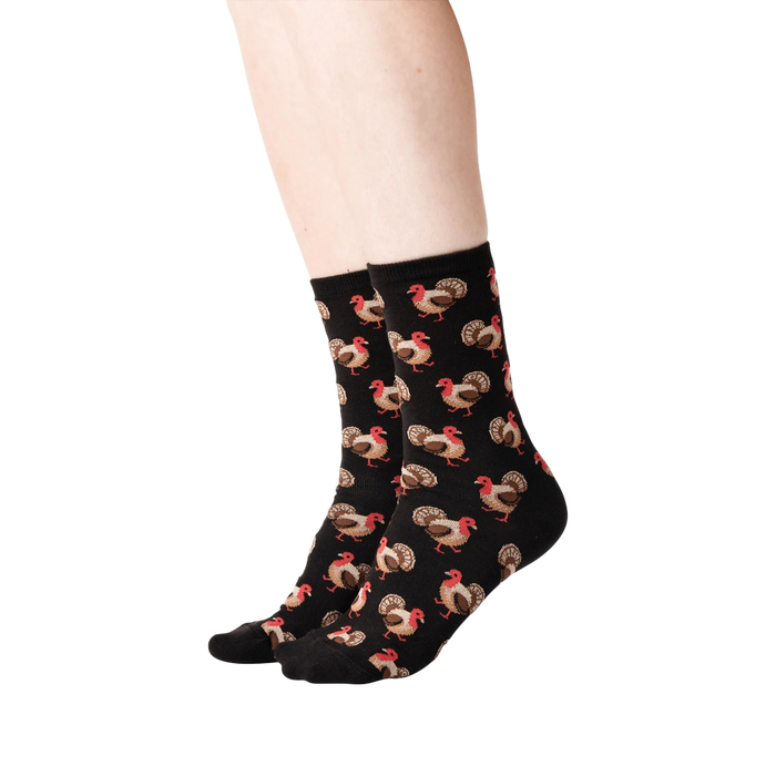Lifestyle shot of a person's legs wearing black crew socks with a repeating pattern of brown and red turkeys.