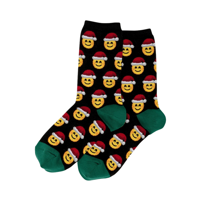 Pair of black crew socks.  Feature a repeating pattern of yellow smiley faces wearing red Santa hats. Green cuffs.