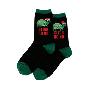 Pair of black crew socks with green cuffs. Design features a green turtle wearing a Santa hat and 'Slow Ho Ho' text.