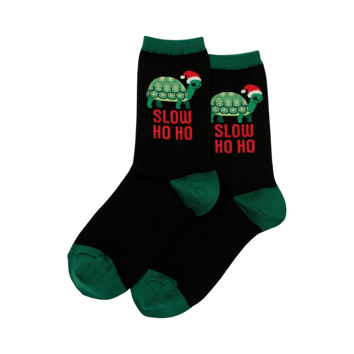 Pair of black crew socks with green cuffs. Design features a green turtle wearing a Santa hat and 'Slow Ho Ho' text.