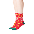 Lifestyle shot showing the socks on a person's feet. The socks are red with gold jingle bells and green cuffs. 
