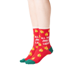 Lifestyle shot showing the socks on a person's feet. The socks are red with gold jingle bells and green cuffs. 