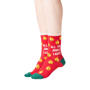 Lifestyle shot showing the socks on a person's feet. The socks are red with gold jingle bells and green cuffs. 