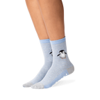 Lifestyle shot showing the penguin socks on a person's legs. The socks are mostly blue and grey, with a subtle striped pattern. A small, embroidered penguin is visible near the ankle area. A good example of how the socks look when worn.