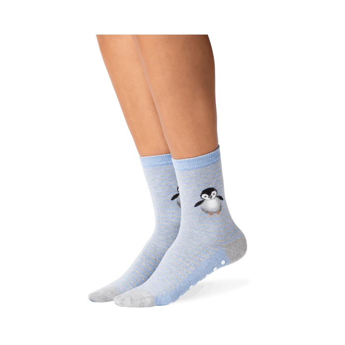 Lifestyle shot showing the penguin socks on a person's legs. The socks are mostly blue and grey, with a subtle striped pattern. A small, embroidered penguin is visible near the ankle area. A good example of how the socks look when worn.