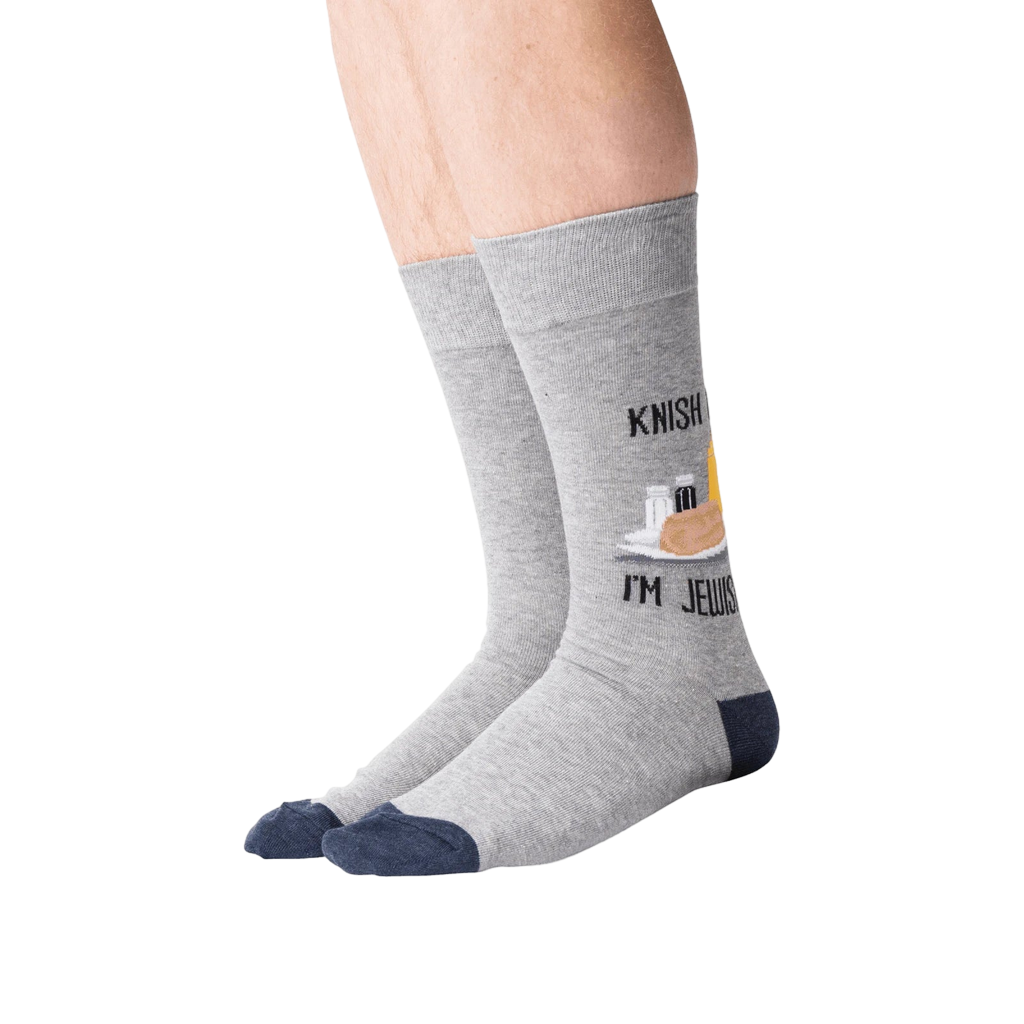Lifestyle shot of a person wearing the 'Knish Me, I'm Jewish' socks. The socks are gray with a navy blue cuff and feature a knish graphic.