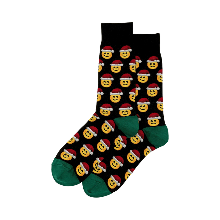 Pair of black crew socks featuring a repeating pattern of yellow smiling emojis wearing Santa hats. Green cuffs.