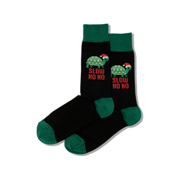 Pair of black crew socks with dark green cuffs, heels, and toes. Features green turtles wearing Santa hats and "SLOW HO HO" text in red.
