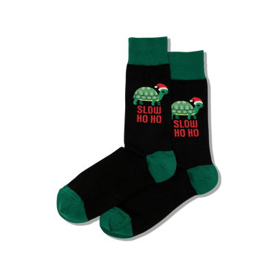 Pair of black crew socks with dark green cuffs, heels, and toes. Features green turtles wearing Santa hats and "SLOW HO HO" text in red.