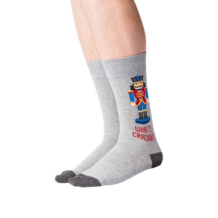 A pair of gray socks with a Nutcracker on them. The Nutcracker is wearing a red and blue outfit and is standing on a brown base. The socks have the words 