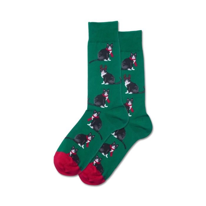 green crew socks with red toes and heels feature a pattern of black cats wearing red scarves and reindeer antlers.   