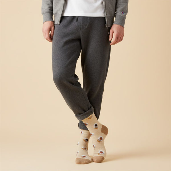 Model wearing beige crew socks with coffee cups, styled with cuffed grey sweatpants & hoodie on a light tan background. [lf]