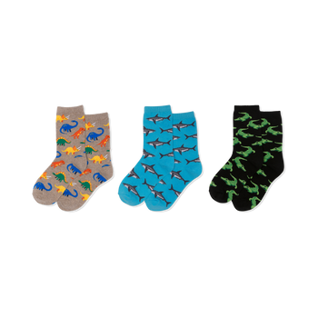 Three pairs of crew socks: one tan with colorful dinosaurs, one blue with grey sharks, and one black with green crocodiles.