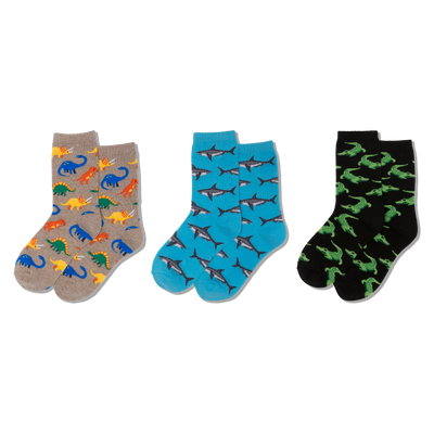 Three pairs of crew socks: one tan with colorful dinosaurs, one blue with grey sharks, and one black with green crocodiles.