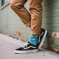 Blue crew socks with skateboarding corgis, styled with cuffed tan pants and black Vans sneakers outdoors. [lf]