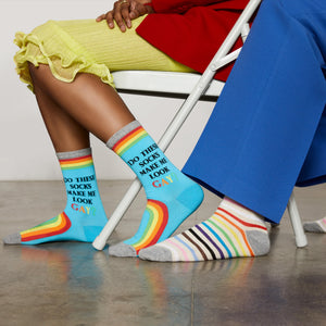Two people are sitting on a chair. The person on the left is wearing a yellow skirt and rainbow socks that say 