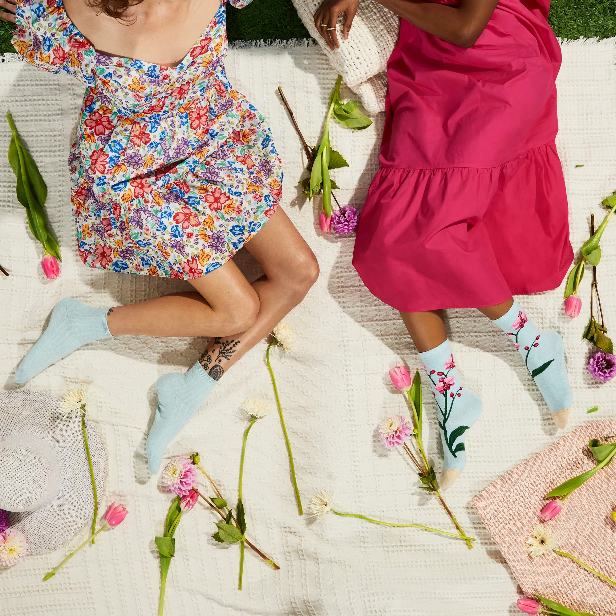 Lifestyle shot of two women wearing Orchid socks, sitting on a blanket surrounded by flowers. [lf]