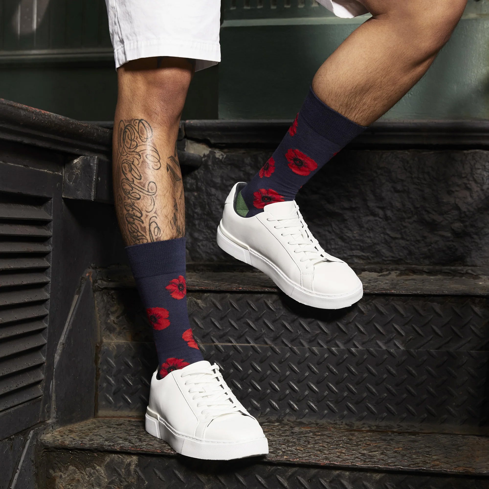 A man's legs wearing navy blue poppy-print crew socks with white sneakers.  Lifestyle shot on a city street. [lf]