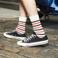 Lifestyle shot: Man wearing cream and red striped socks with black Converse sneakers. [lf]