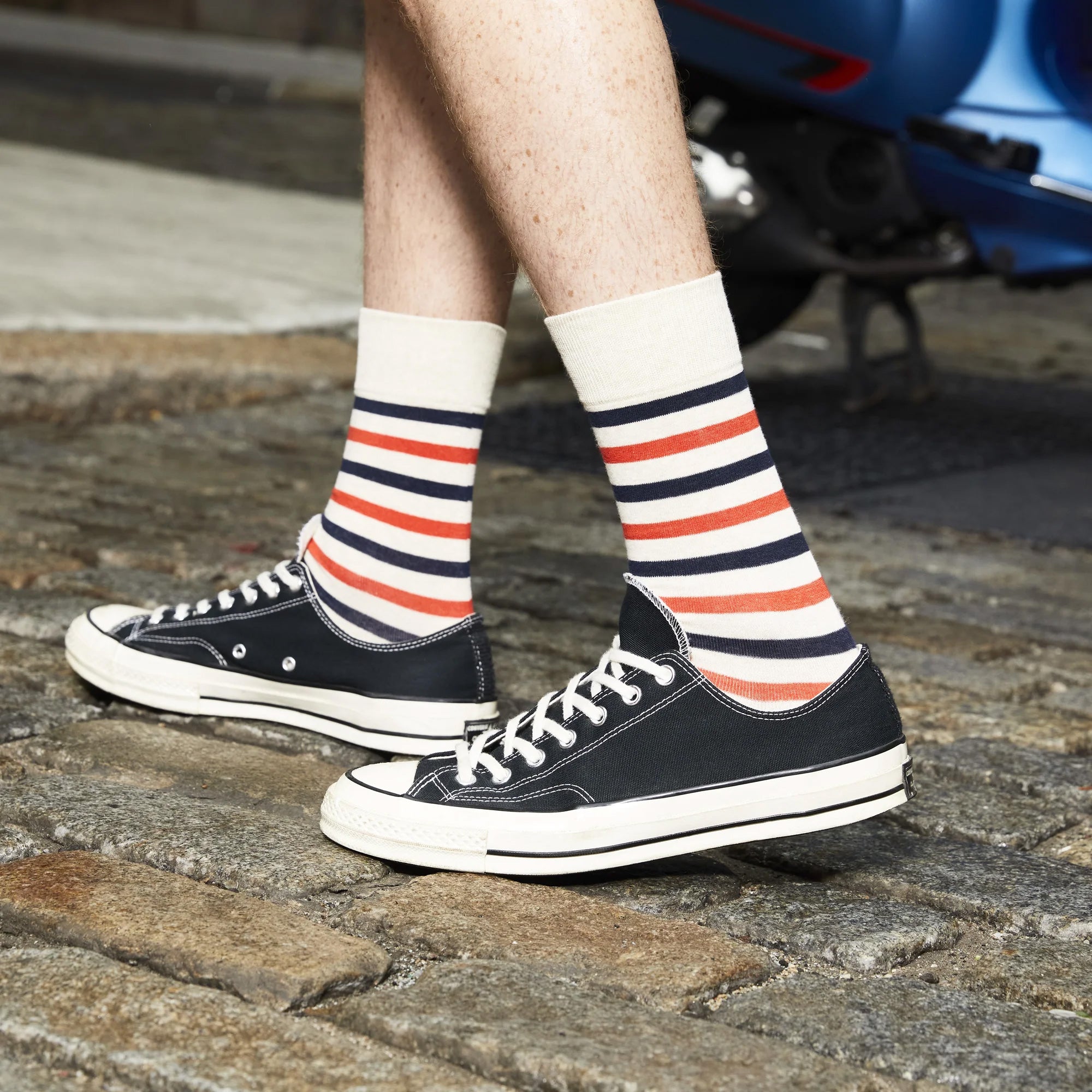 Lifestyle shot: Man wearing cream and red striped socks with black Converse sneakers. [lf]