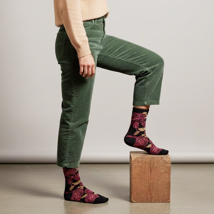 Model wearing beige sweater, green corduroys, and black crew socks with bold maroon floral print in studio. [lf]