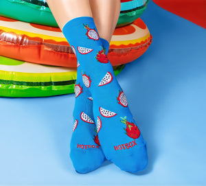 A pair of blue socks with a pattern of dragon fruit slices. The socks are pulled up to the mid-calf of a model sitting on a stack of inflatable pool floats.