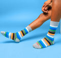 Lifestyle shot of a person's legs wearing gray ombre stripe crew socks against a blue background. [lf]