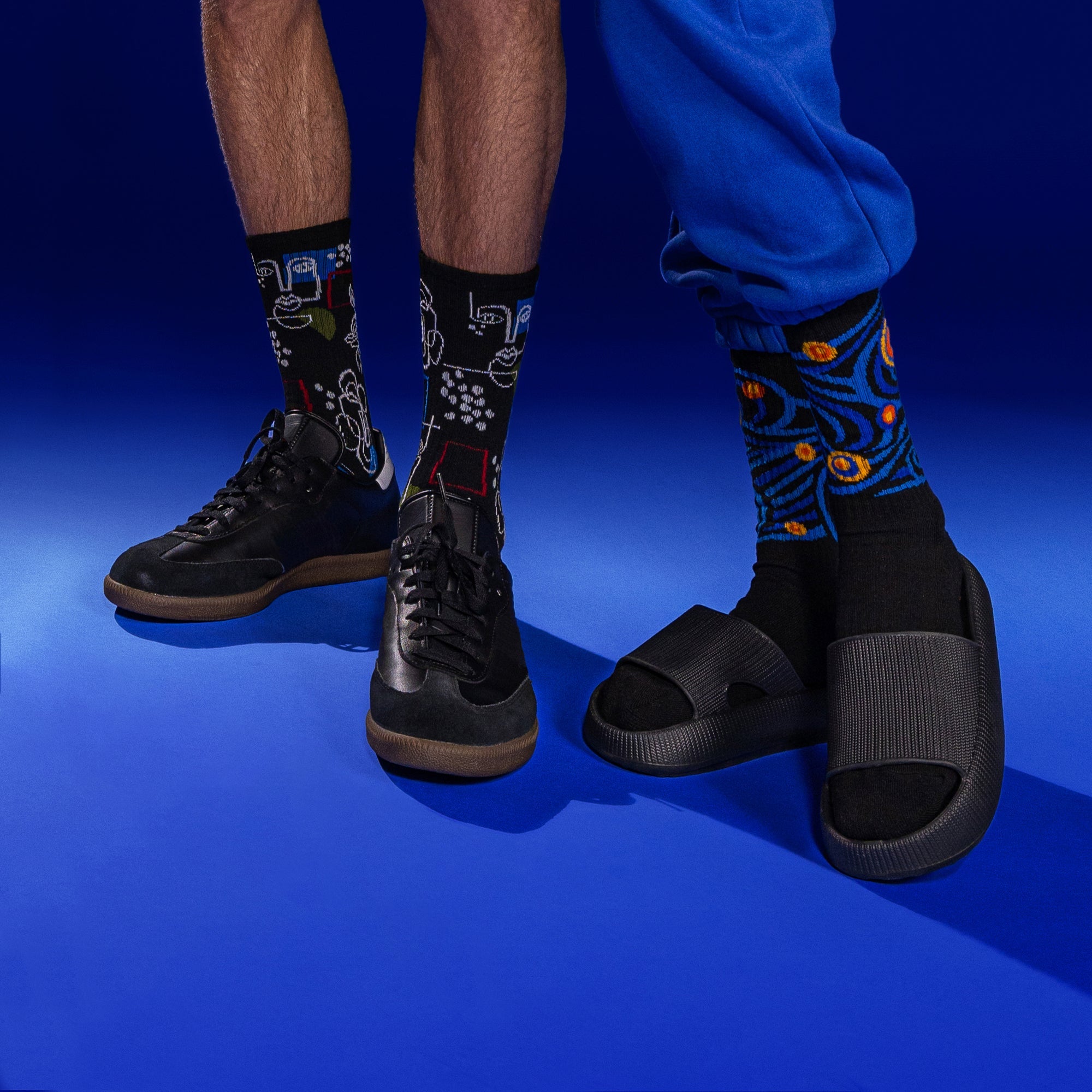 Lifestyle shot showing two people wearing different patterned socks; one is wearing the Art Faces socks with black shoes, the other is wearing orange socks with black slides. Both are shown against a blue background. [lf]
