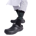 Person wearing "YES, CHEF" black socks with black chef clogs and striped pants, seated on a light wooden block.