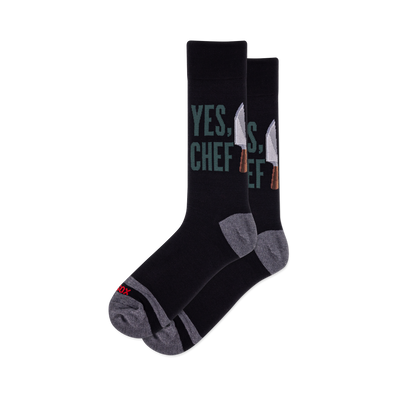 Pair of black crew socks featuring "YES, CHEF" in green text and silver chef knives. Grey heel, toe, and arch details.