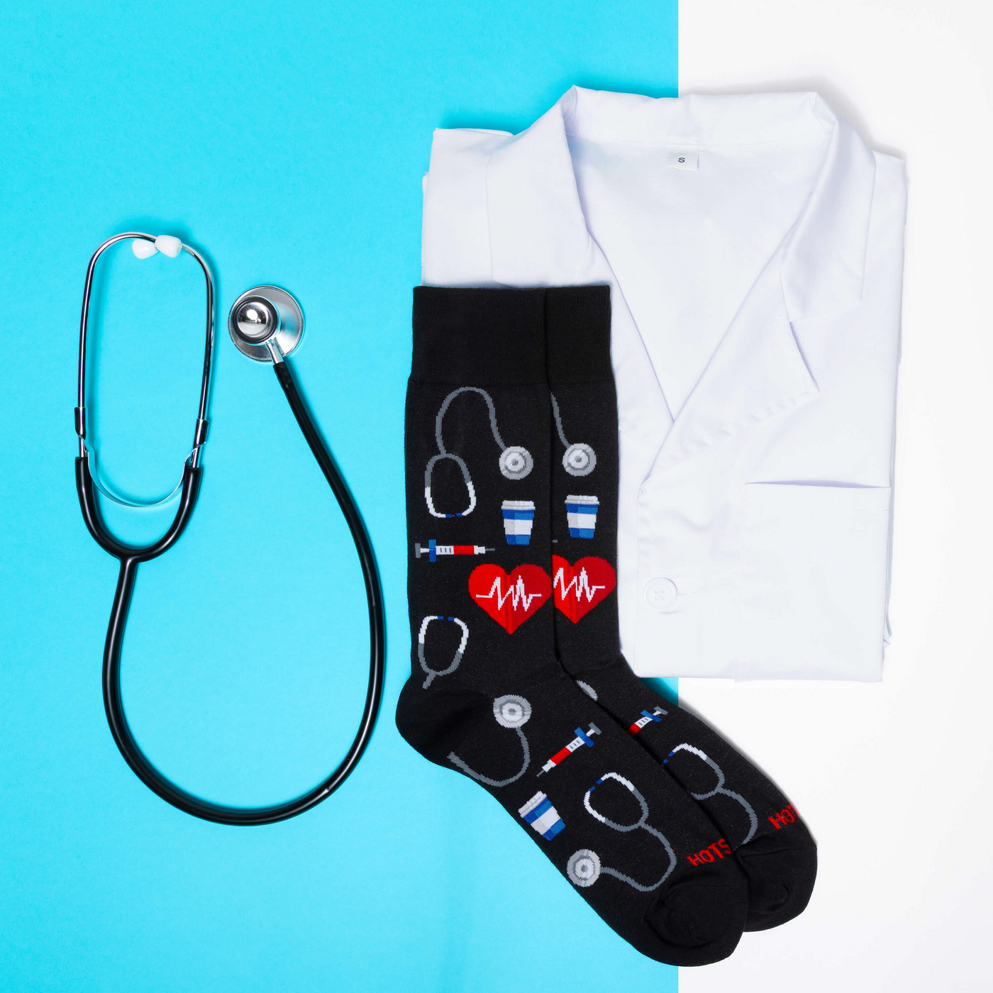 [lf] Black socks with medical patterns, stethoscope, and white lab coat on blue and white background.