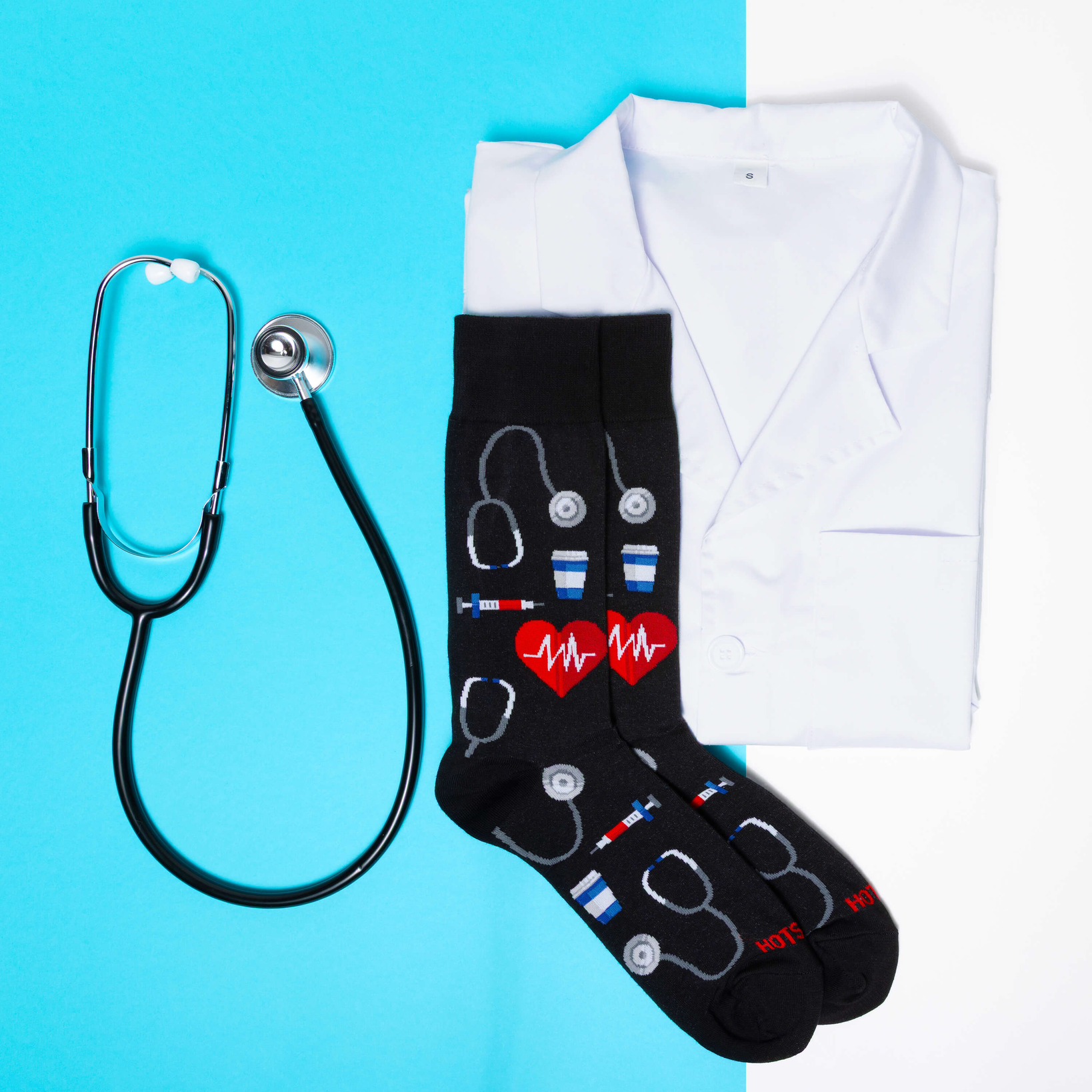 [lf] Black socks with medical patterns, stethoscope, and white lab coat on blue and white background.