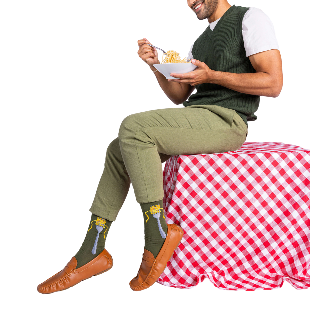 Man in olive green pants and sweater vest, sitting and eating spaghetti, wearing olive green socks with a fork design.