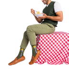 Man in olive green pants and sweater vest, sitting and eating spaghetti, wearing olive green socks with a fork design.