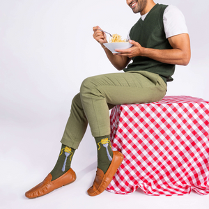 Man in olive green pants and sweater vest, sitting and eating spaghetti, wearing olive green socks with a fork design.