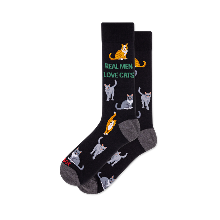 Pair of black crew socks with grey heel and toe. Features green text 'REAL MEN LOVE CATS' and an all-over pattern of grey and orange tabby cats. }}